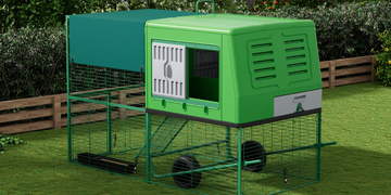 Green plastic chicken coop with wheels on a grassy area